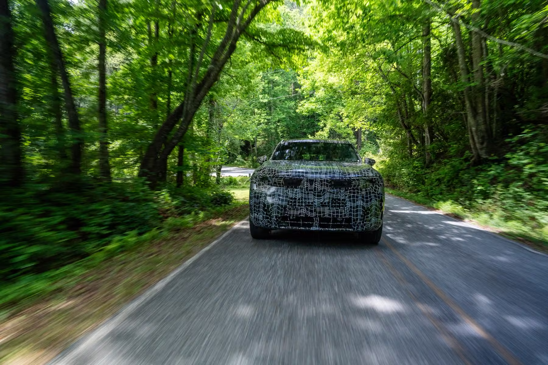 Novo BMW X5 camuflado visto de frente em estrada estreita entre árvores