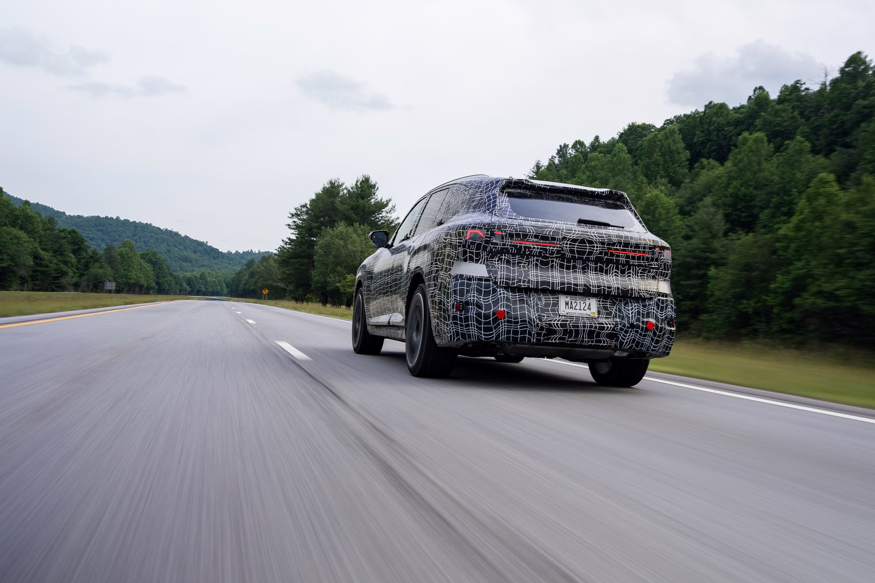 Novo BMW X5 camuflado visto de traseira em rodovia com montanhas ao fundo