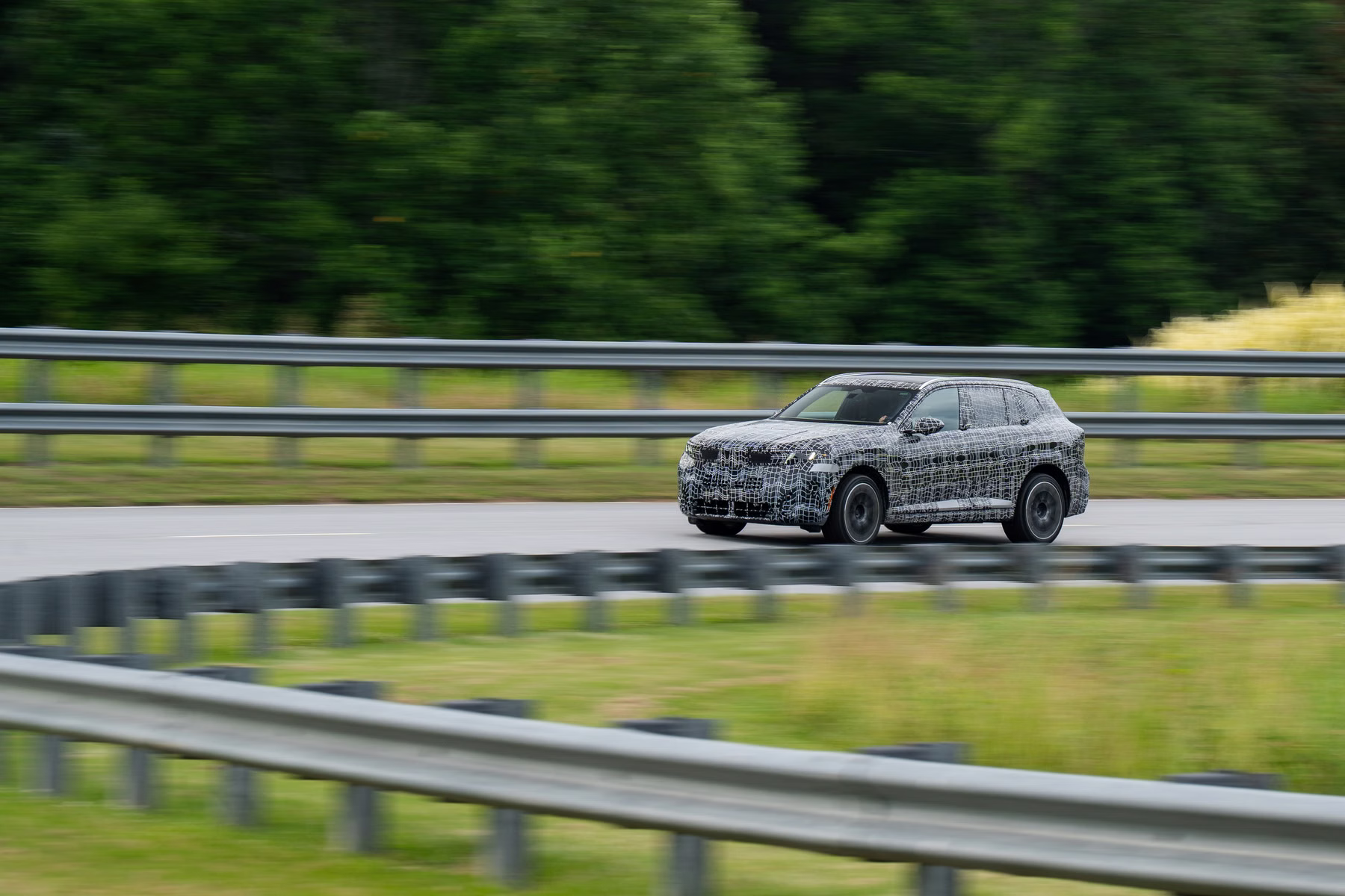 Novo BMW X5 camuflado em movimento lateral atrás de guard-rail