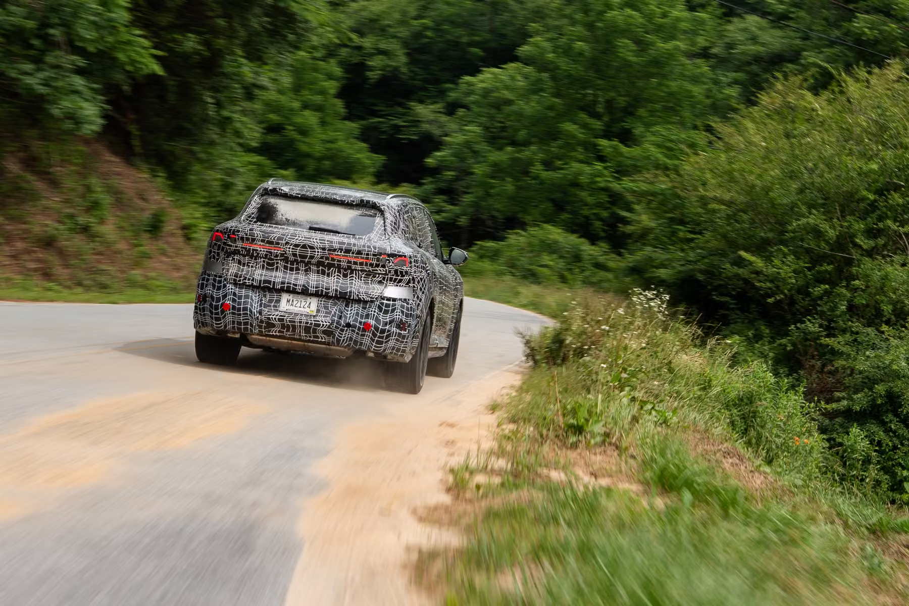 Novo BMW X5 camuflado em curva de estrada com poeira na margem