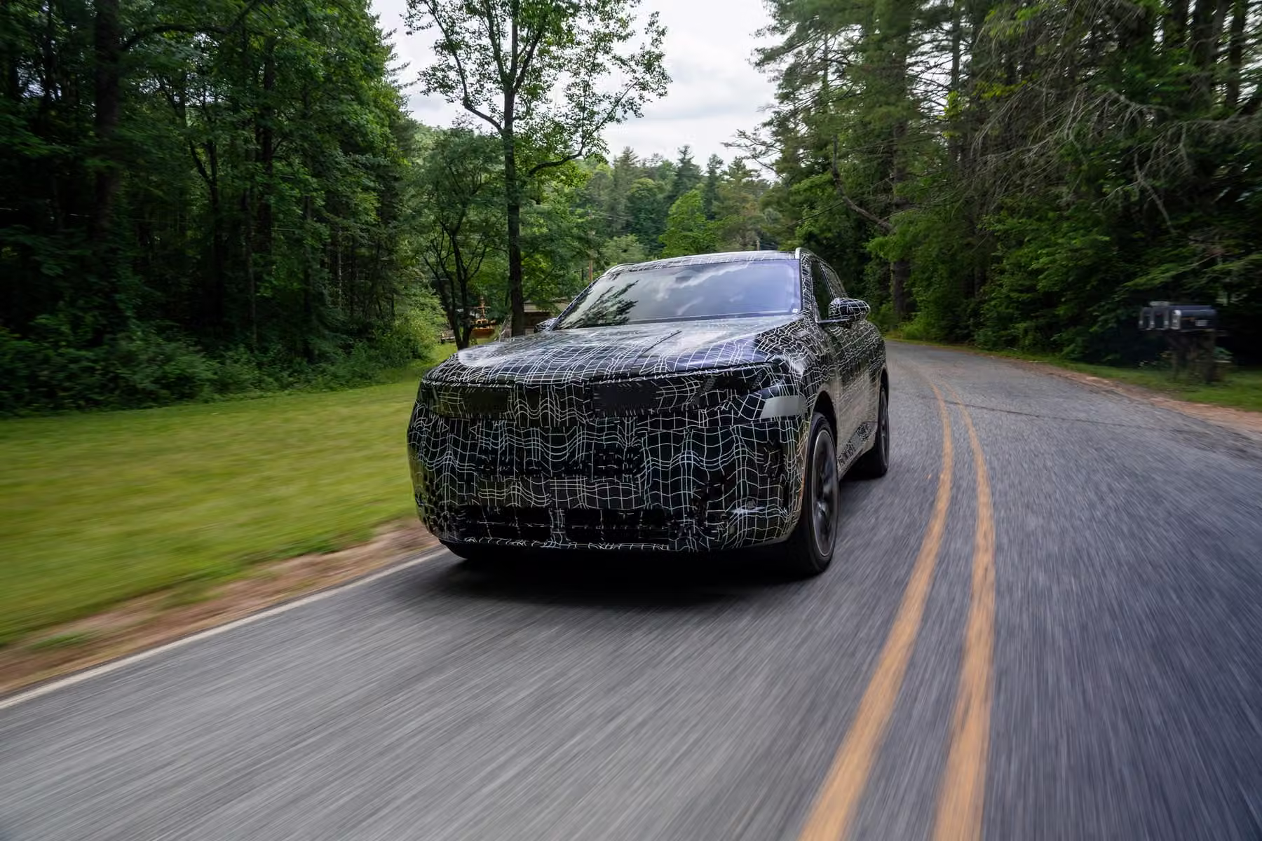 Novo BMW X5 camuflado em estrada de duas faixas cercada por vegetação