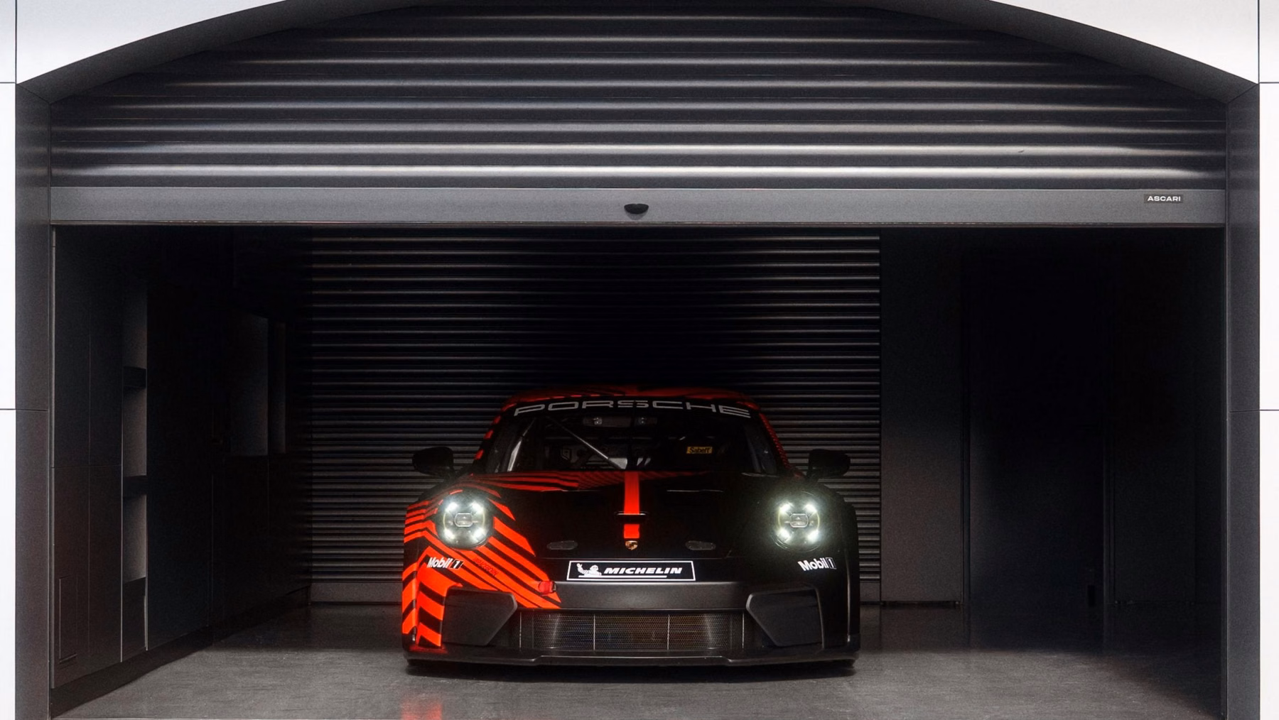 Porsche 911 GT4 R de frente dentro do box com faróis acesos