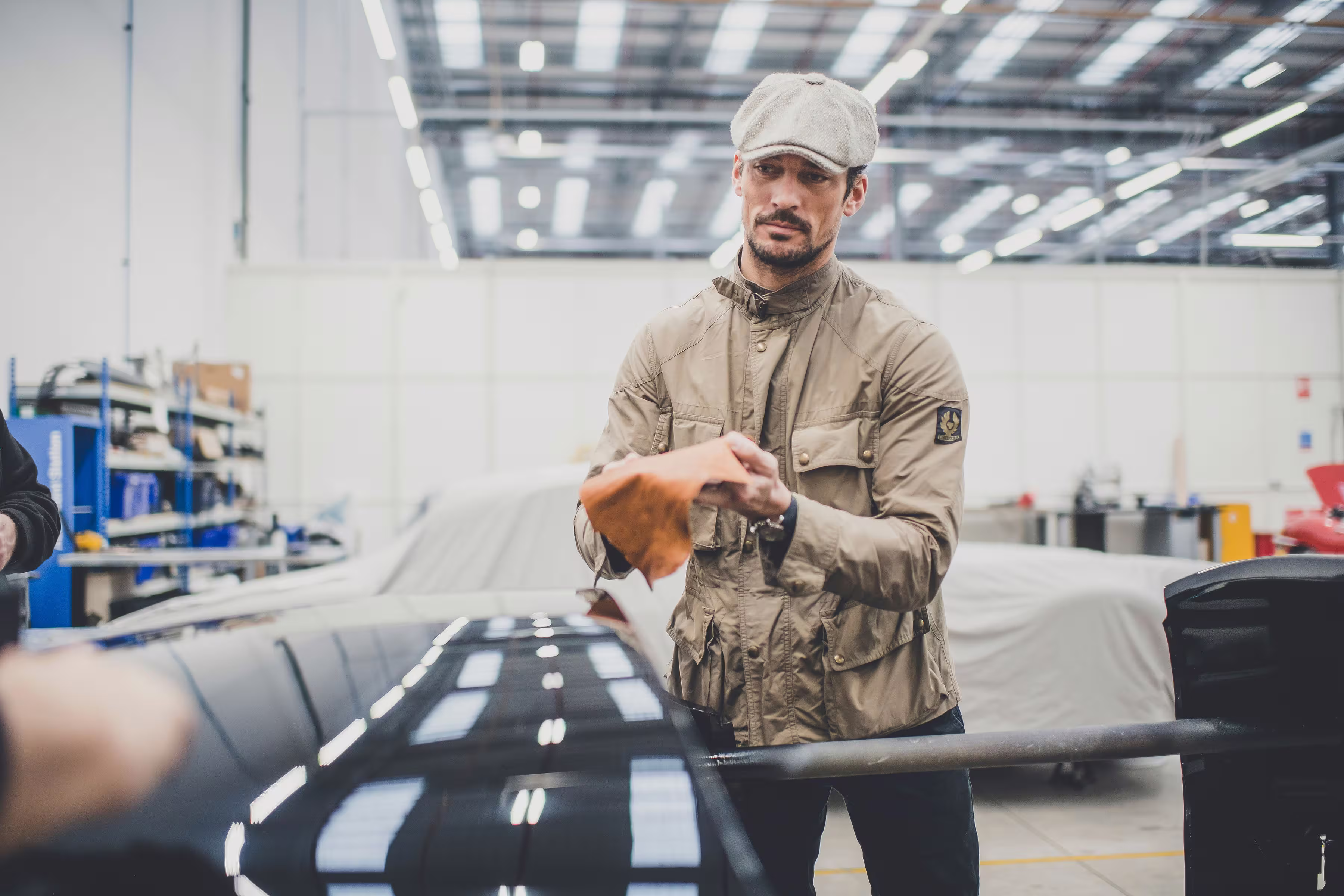 David Gandy segurando amostra de couro ao lado do Jaguar XK120 na oficina