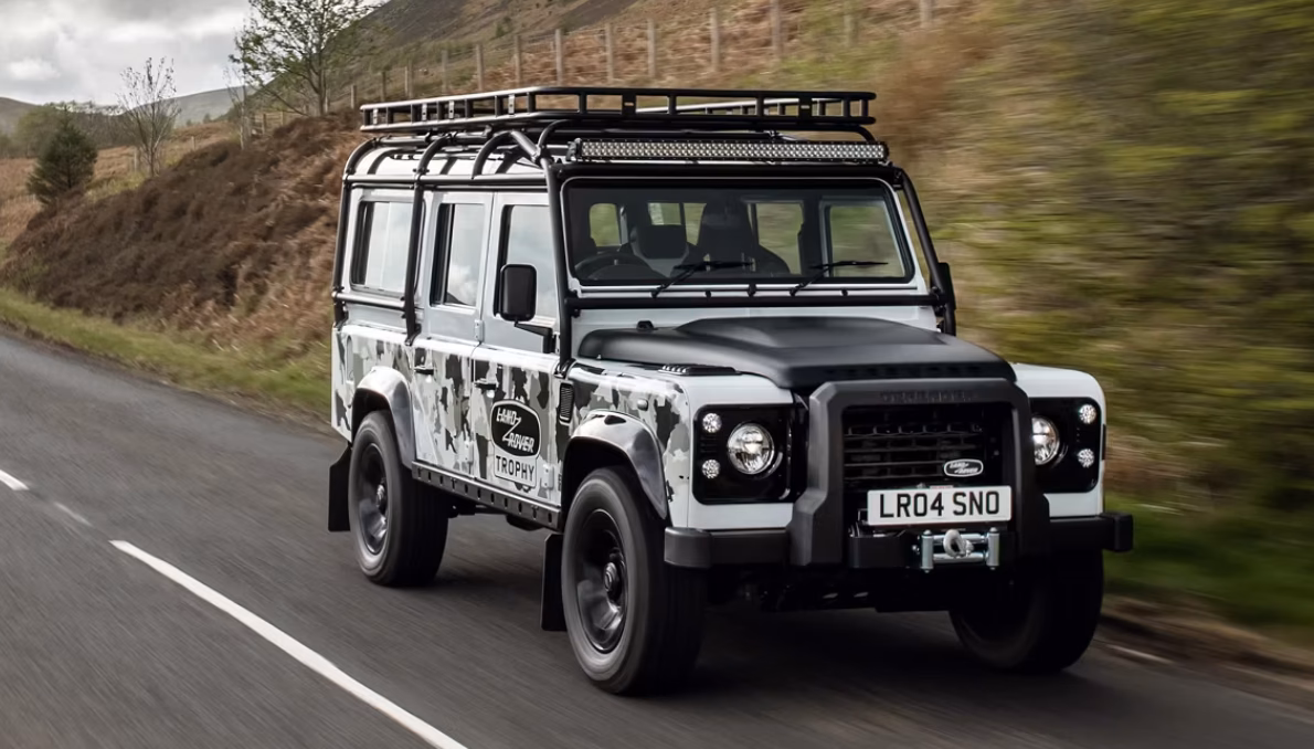 Defender Works V8 Trophy II em movimento em estrada aberta com rack de teto e faróis auxiliares