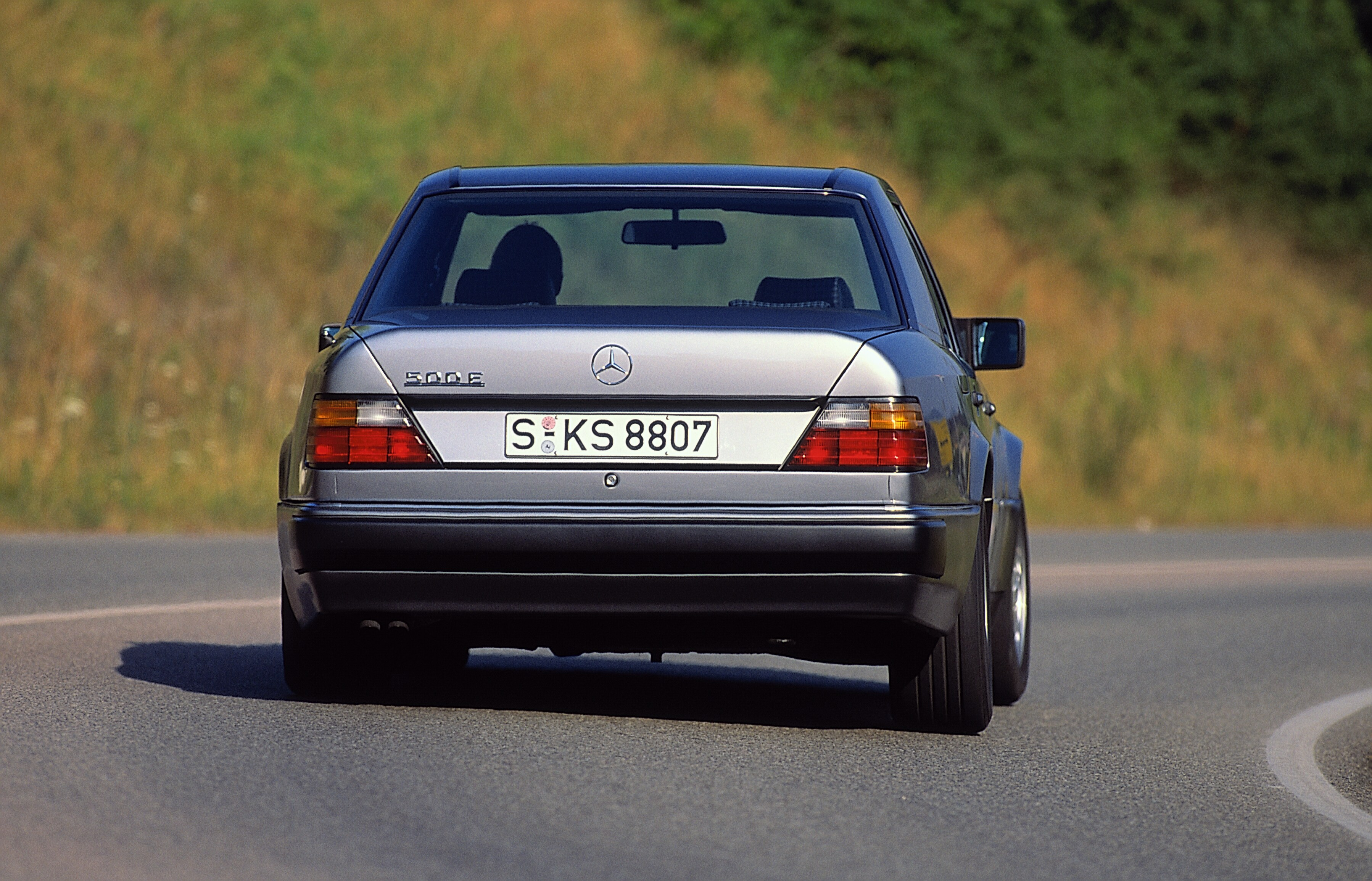 Foto de divulgação de 1990 do Mercedes-Benz 500 E visto pela traseira em movimento