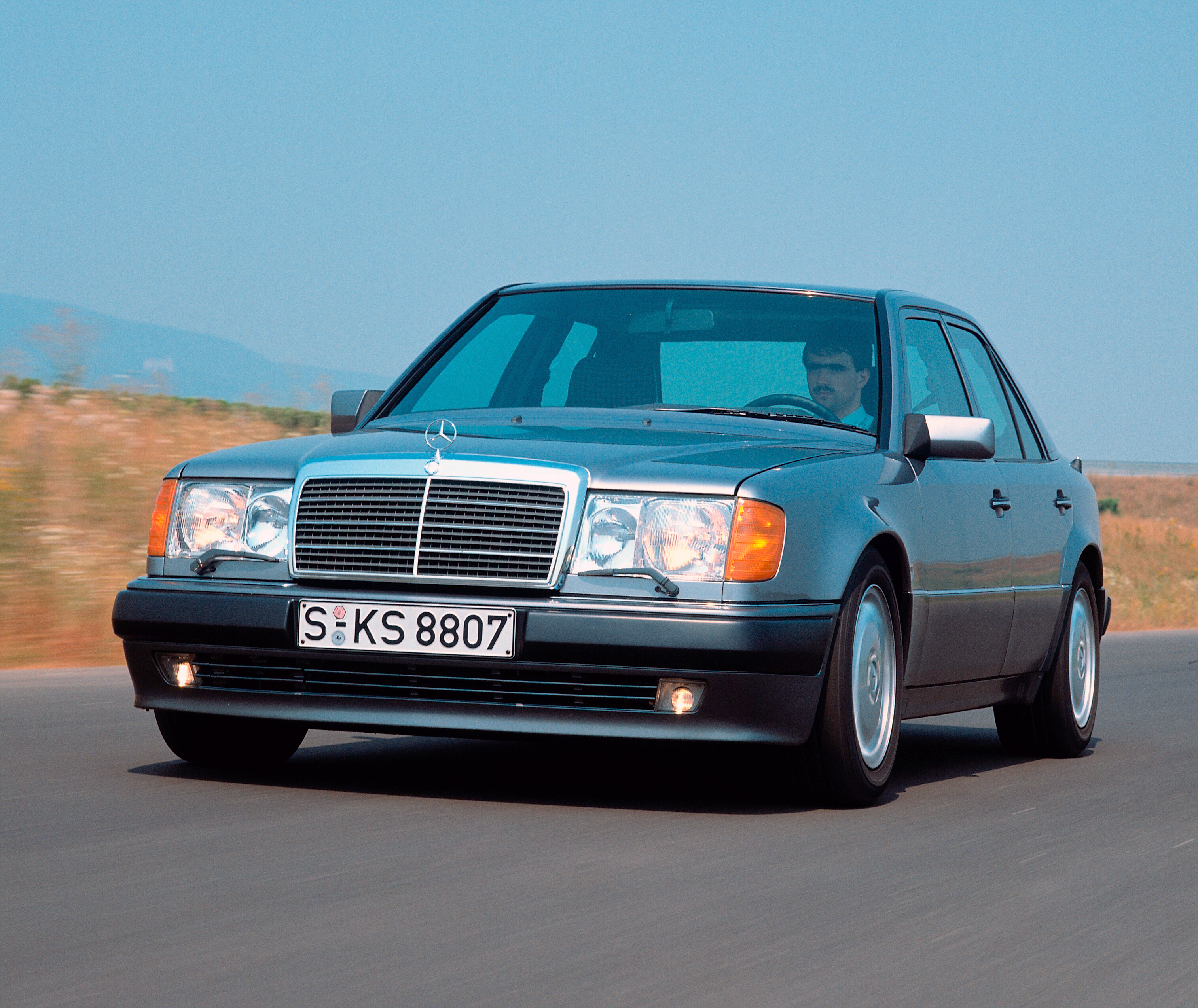 Foto de divulgação de 1990 de um Mercedes-Benz 500 E cinza visto em três quartos dianteiros