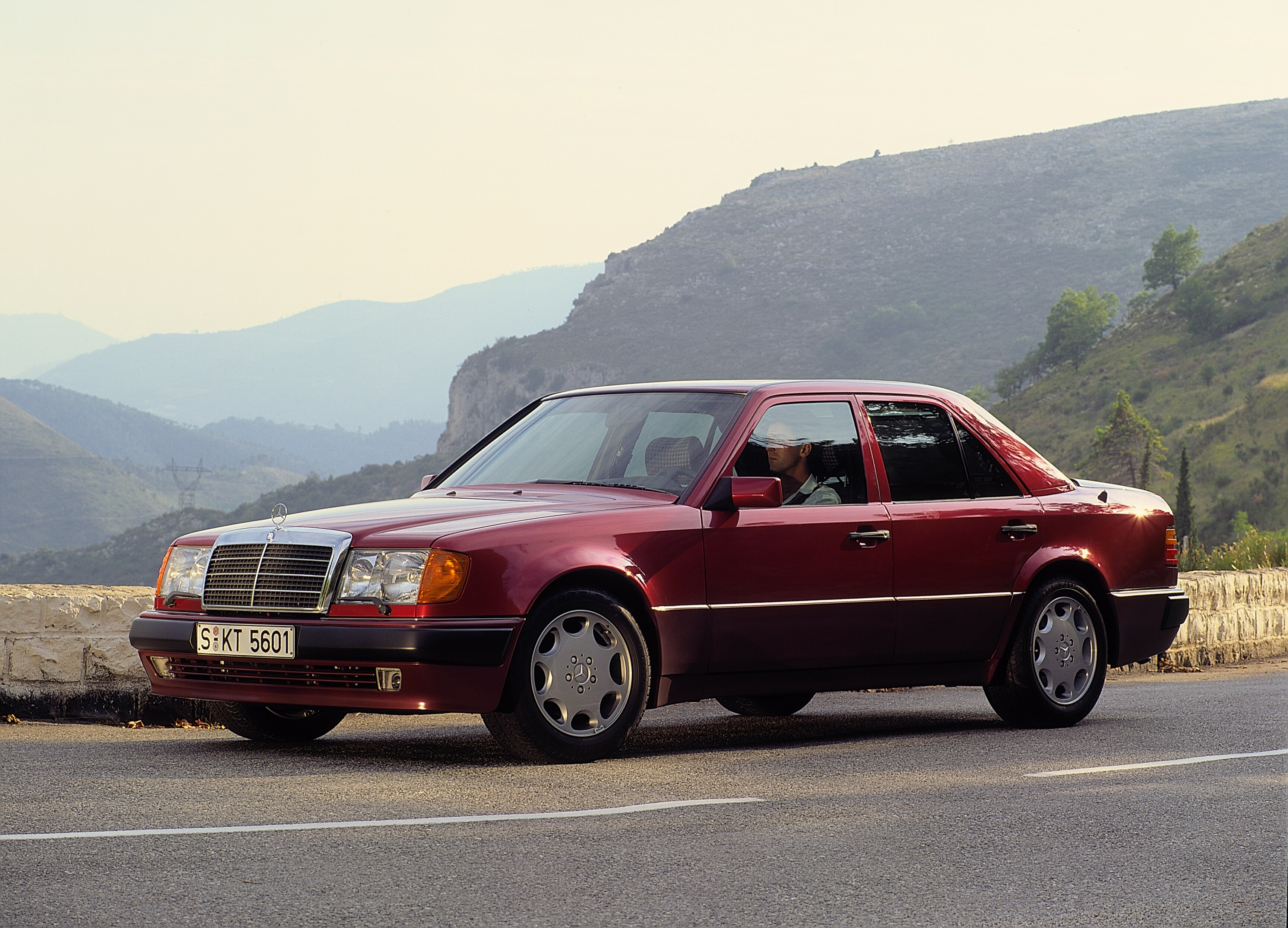 Foto de divulgação de 1990 de um Mercedes-Benz 500 E vermelho diante de uma paisagem montanhosa