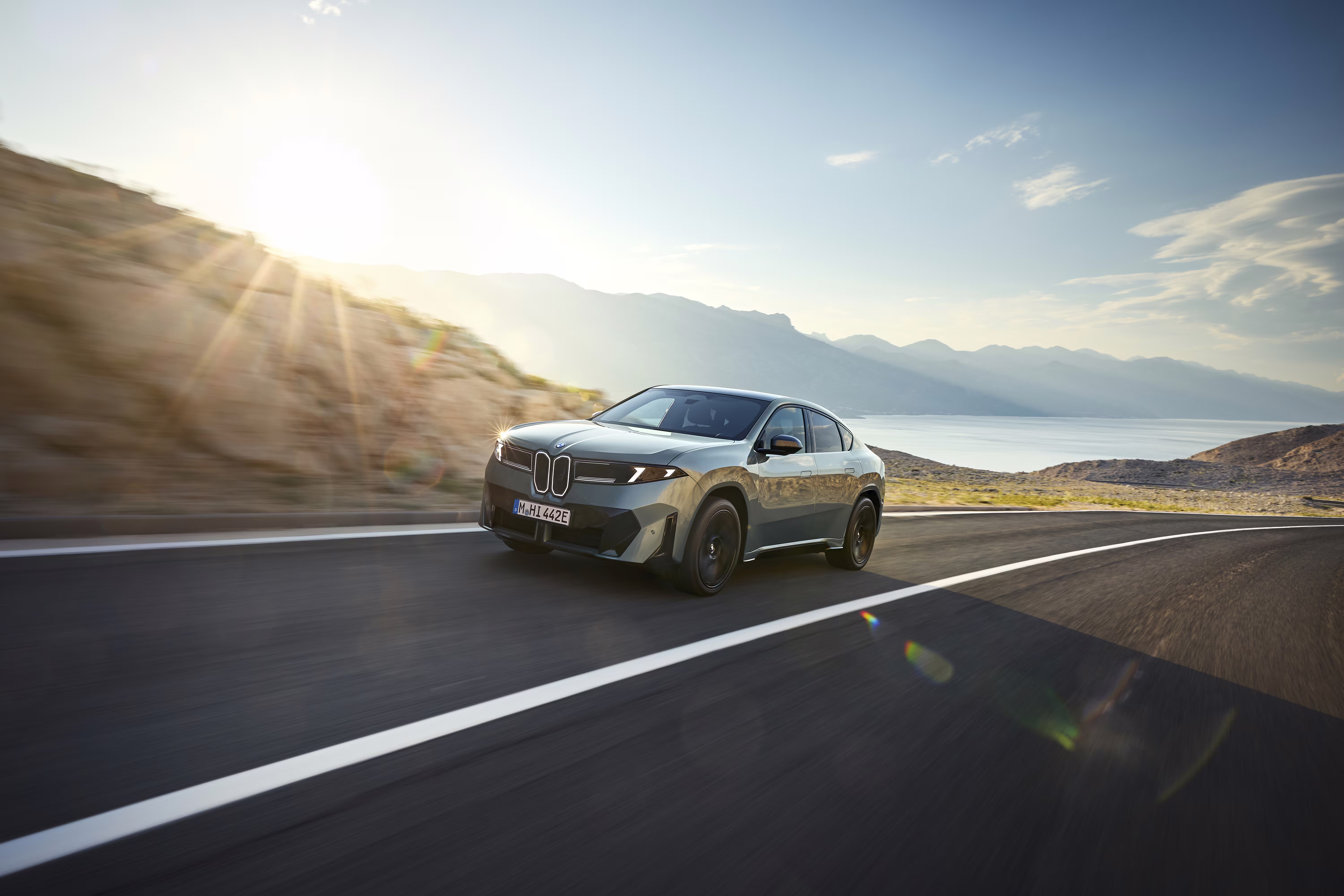 Foto de divulgação da BMW: Outro enquadramento frontal do 50 xDrive junto ao lago, mostrando a carroceria sob luz lateral.