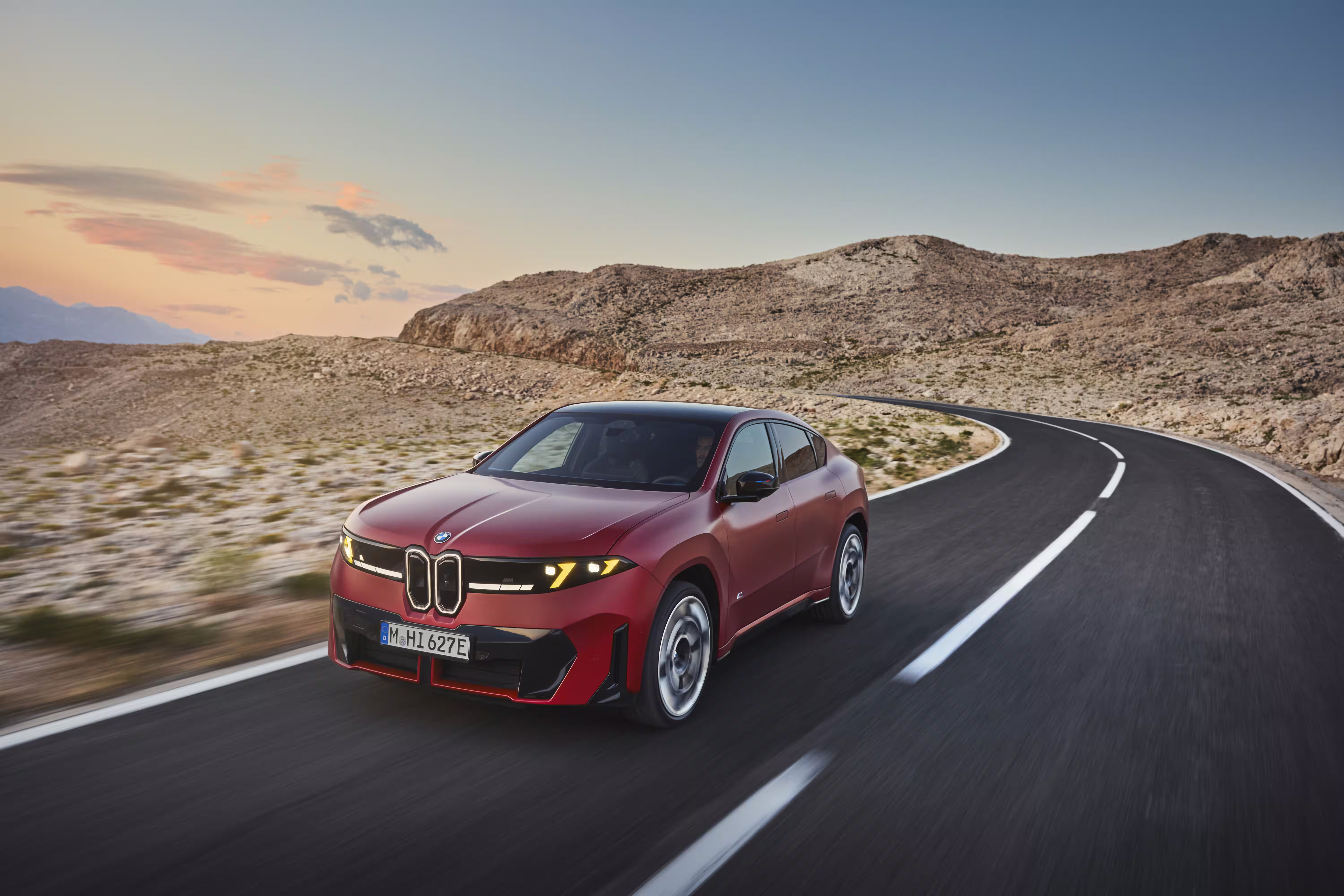 Foto de divulgação da BMW: Vista frontal em três quartos durante uma curva, com a carroceria vermelha acompanhando o relevo da estrada.