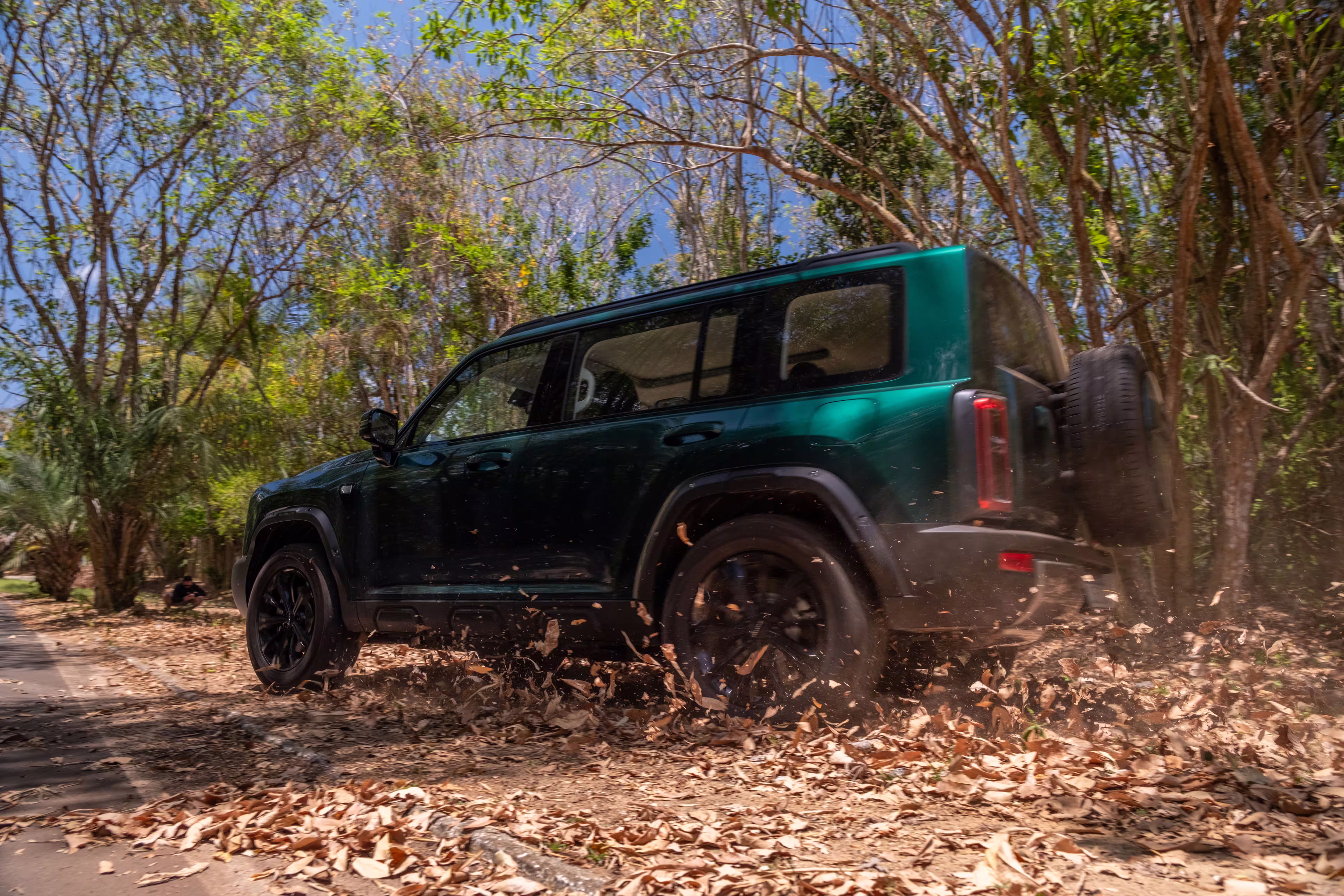 Foto de divulgação do Haval H7 verde avançando por uma trilha cercada de árvores e folhas.