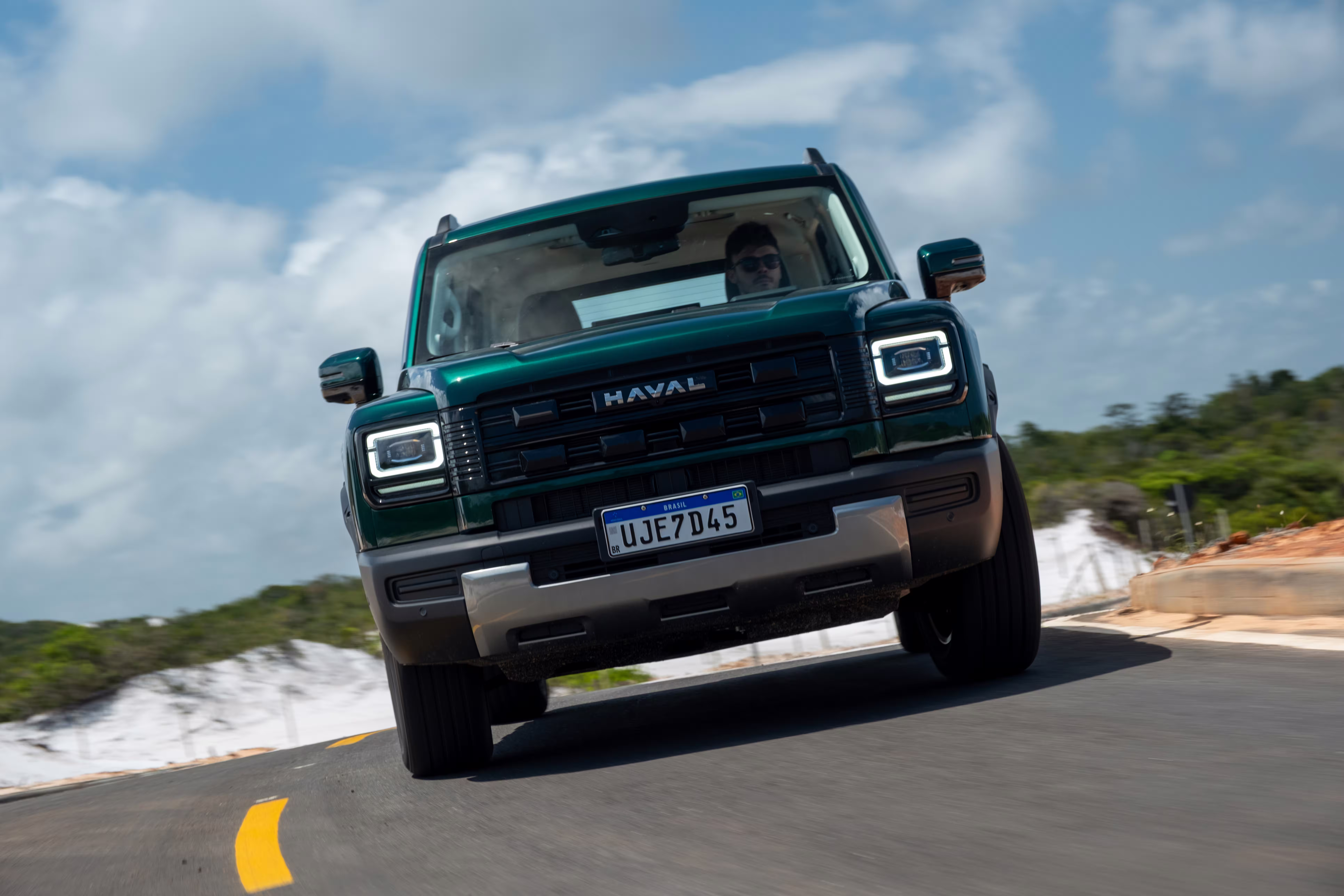Foto de divulgação: Haval H7 verde visto de frente em movimento sobre asfalto, com céu nublado ao fundo.