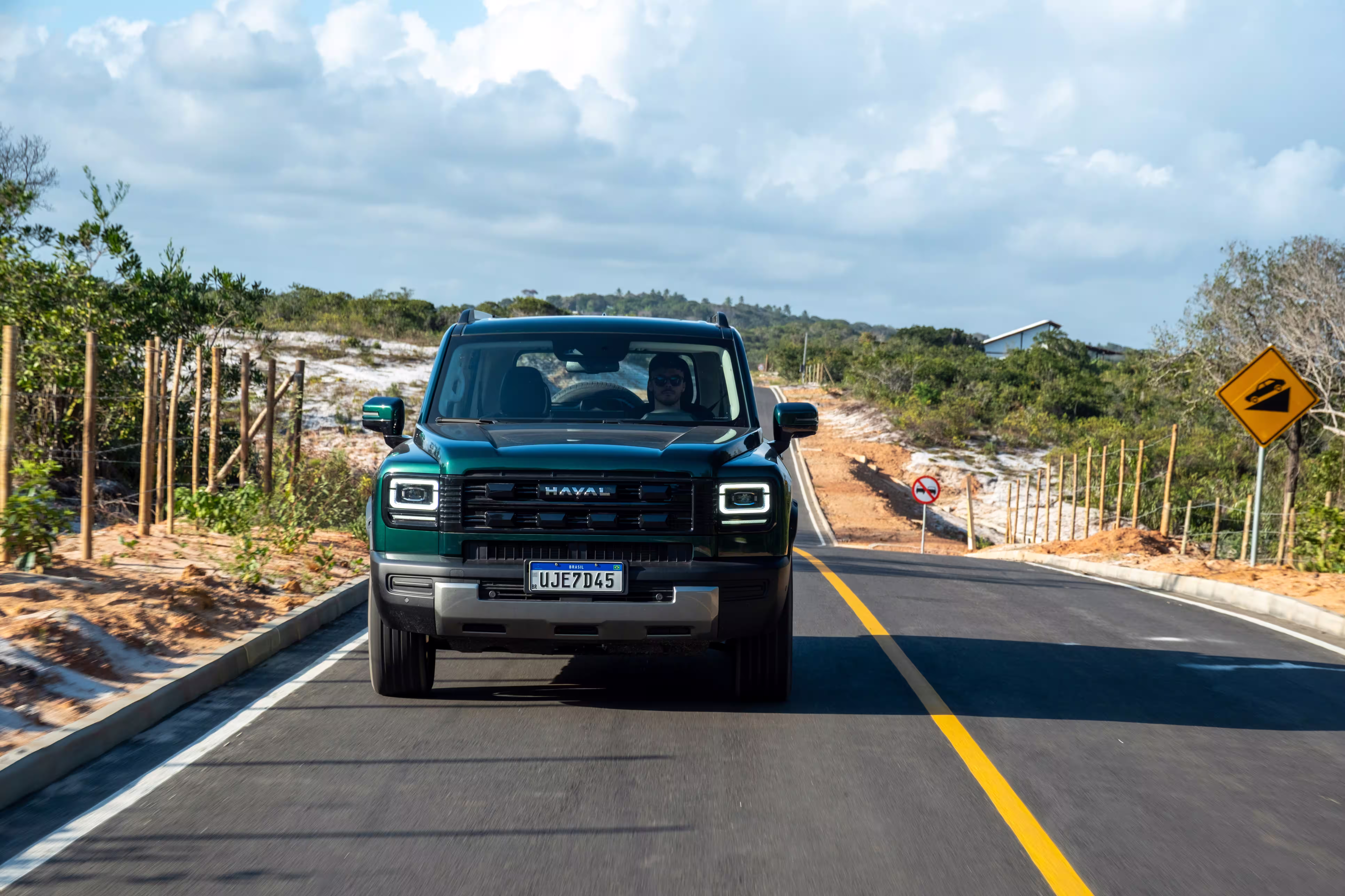 Foto de divulgação: Haval H7 verde de frente numa estrada de asfalto com linha amarela e sinalização ao fundo.
