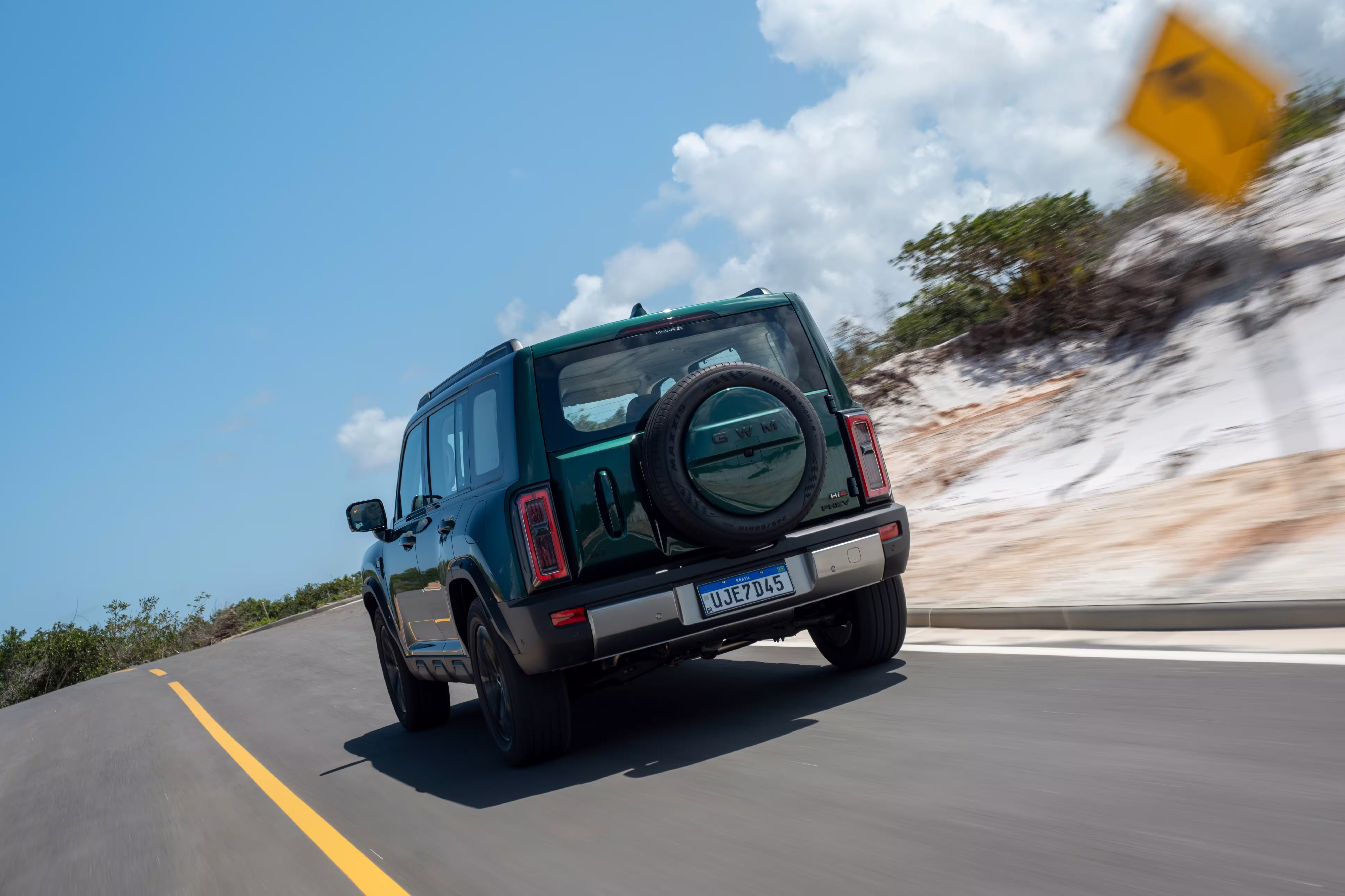 Foto de divulgação: Haval H7 verde de traseira numa curva asfaltada, junto a uma placa de sinalização.