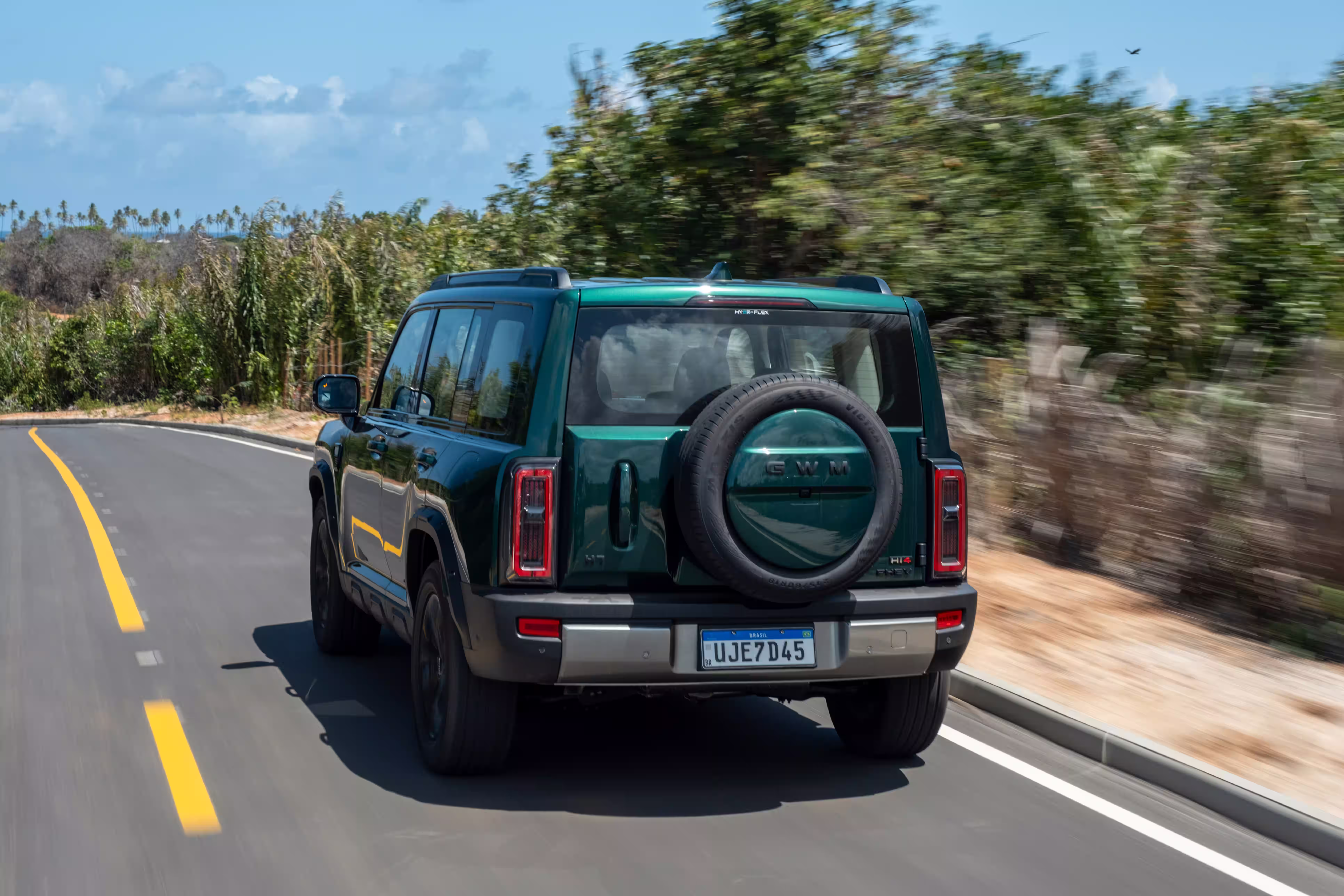 Foto de divulgação: Haval H7 verde visto de trás numa faixa de asfalto com vegetação nas laterais.