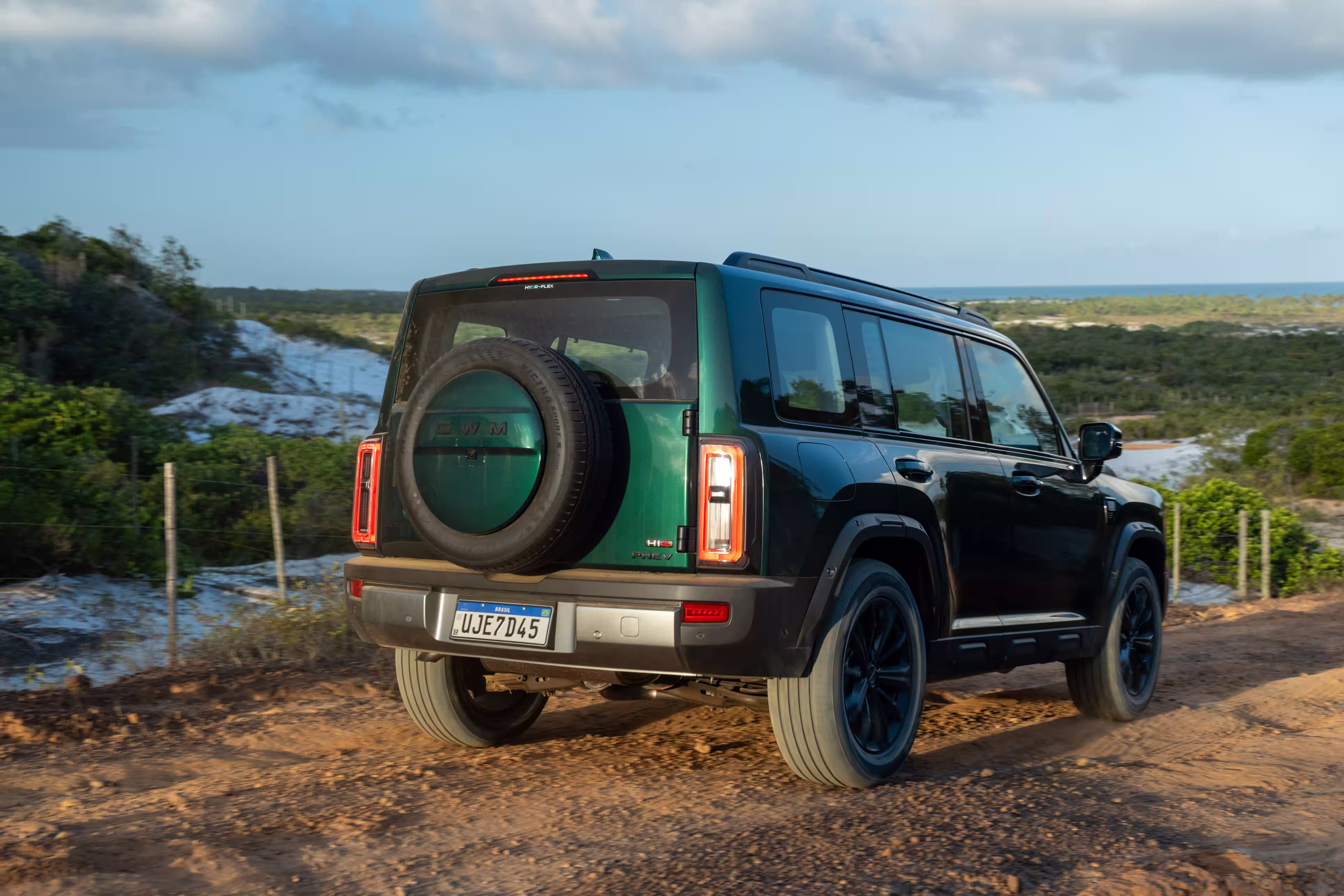 Foto de divulgação: Haval H7 verde visto pela traseira em três quartos numa trilha de terra, com o mar ao fundo.