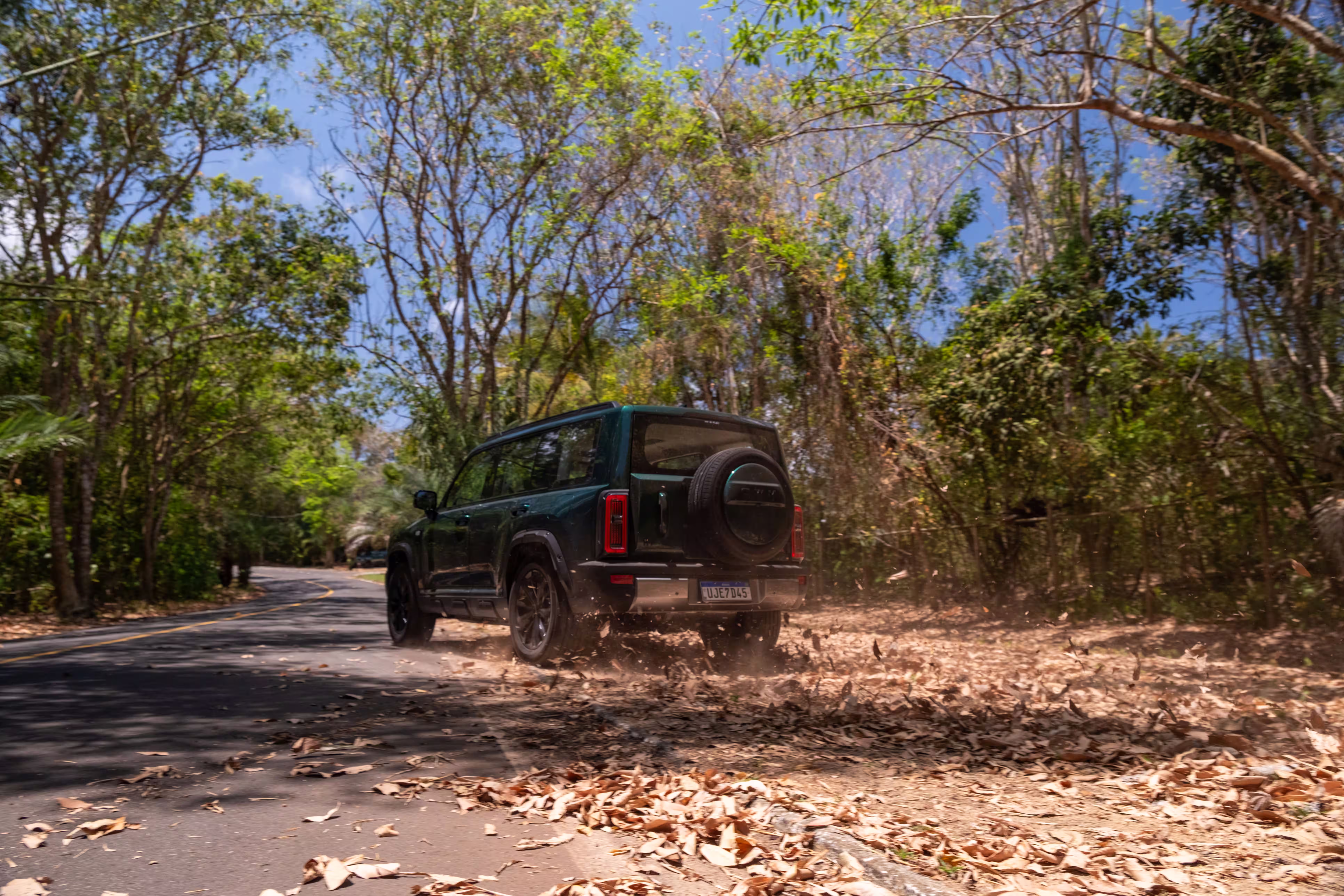 Foto de divulgação: Haval H7 verde visto pela traseira, levantando poeira e folhas numa passagem de terra.
