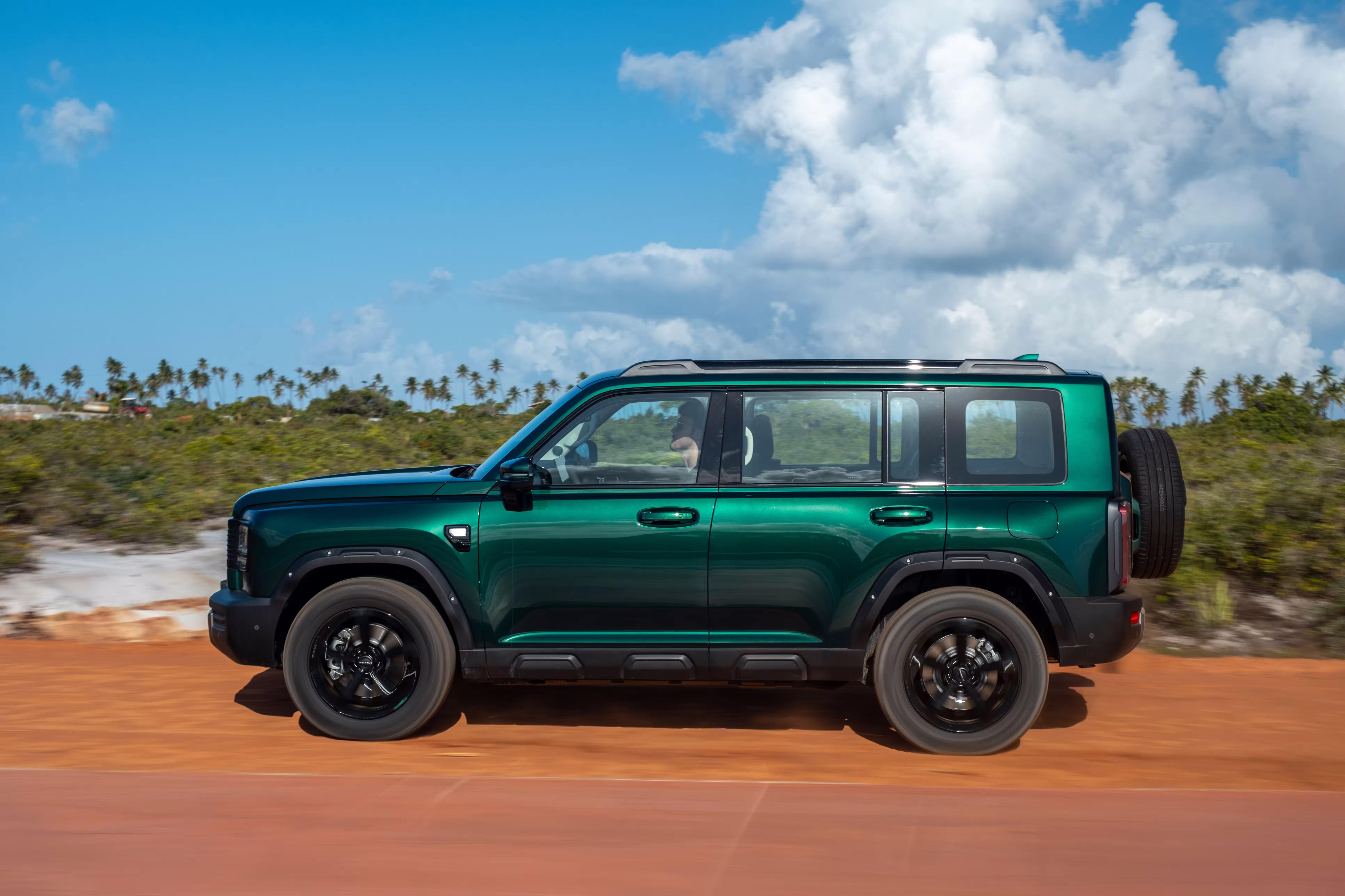 Foto de divulgação do Haval H7 verde em movimento, de perfil, junto a uma paisagem litorânea.
