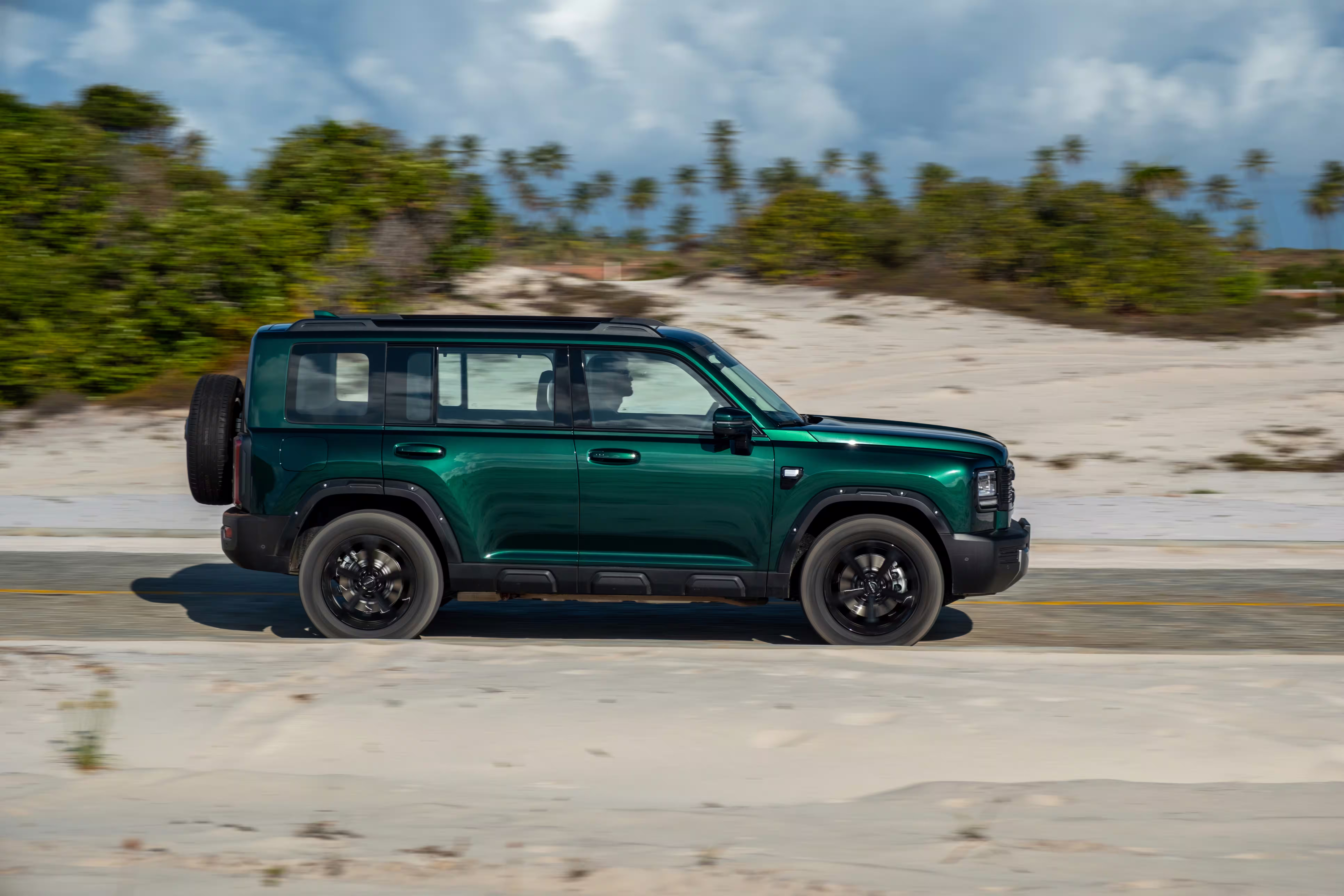 Foto de divulgação: Haval H7 verde de perfil em movimento numa estrada costeira.