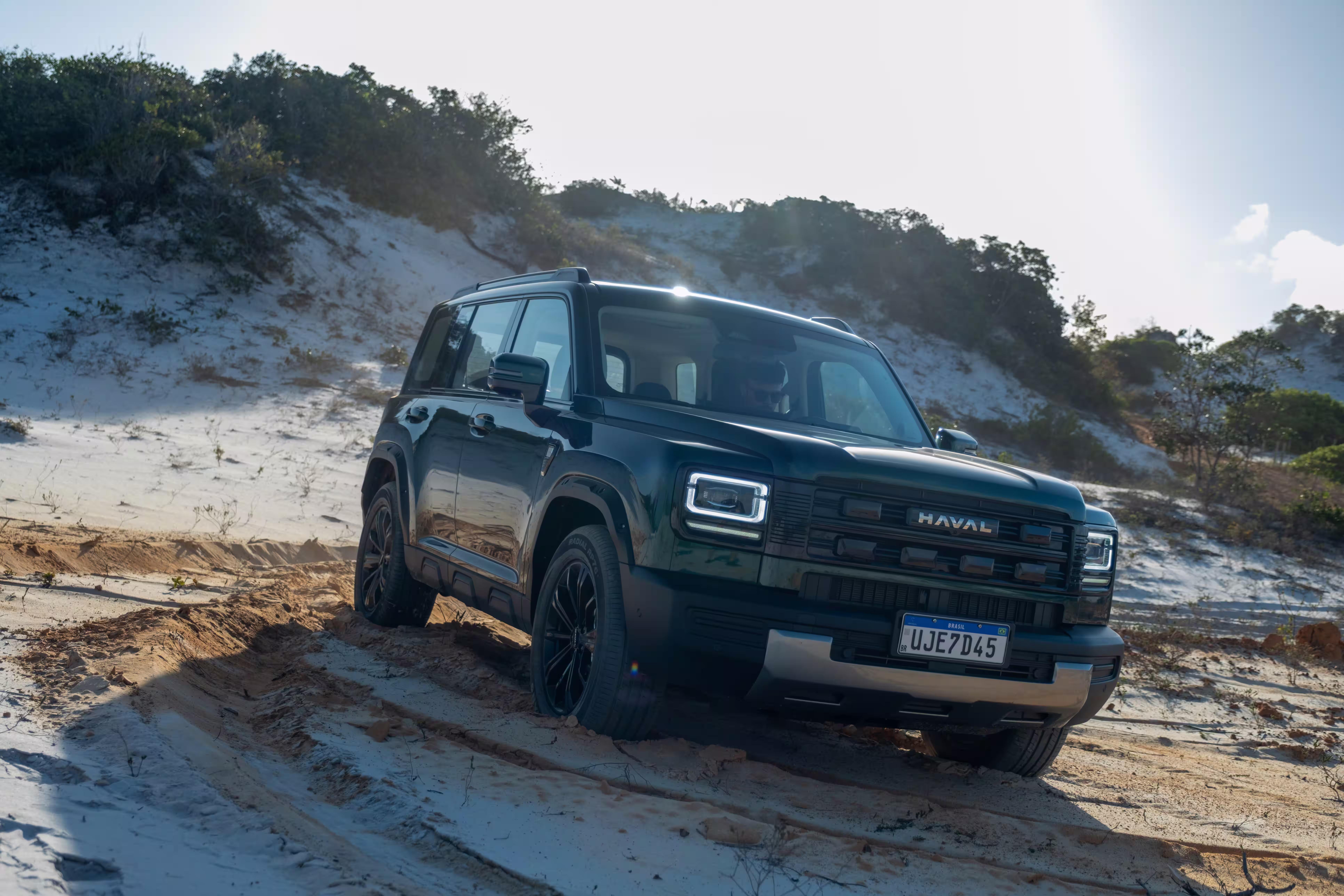 Foto de divulgação: Haval H7 verde em três quartos dianteiros sobre um trecho de areia com marcas de pneus.