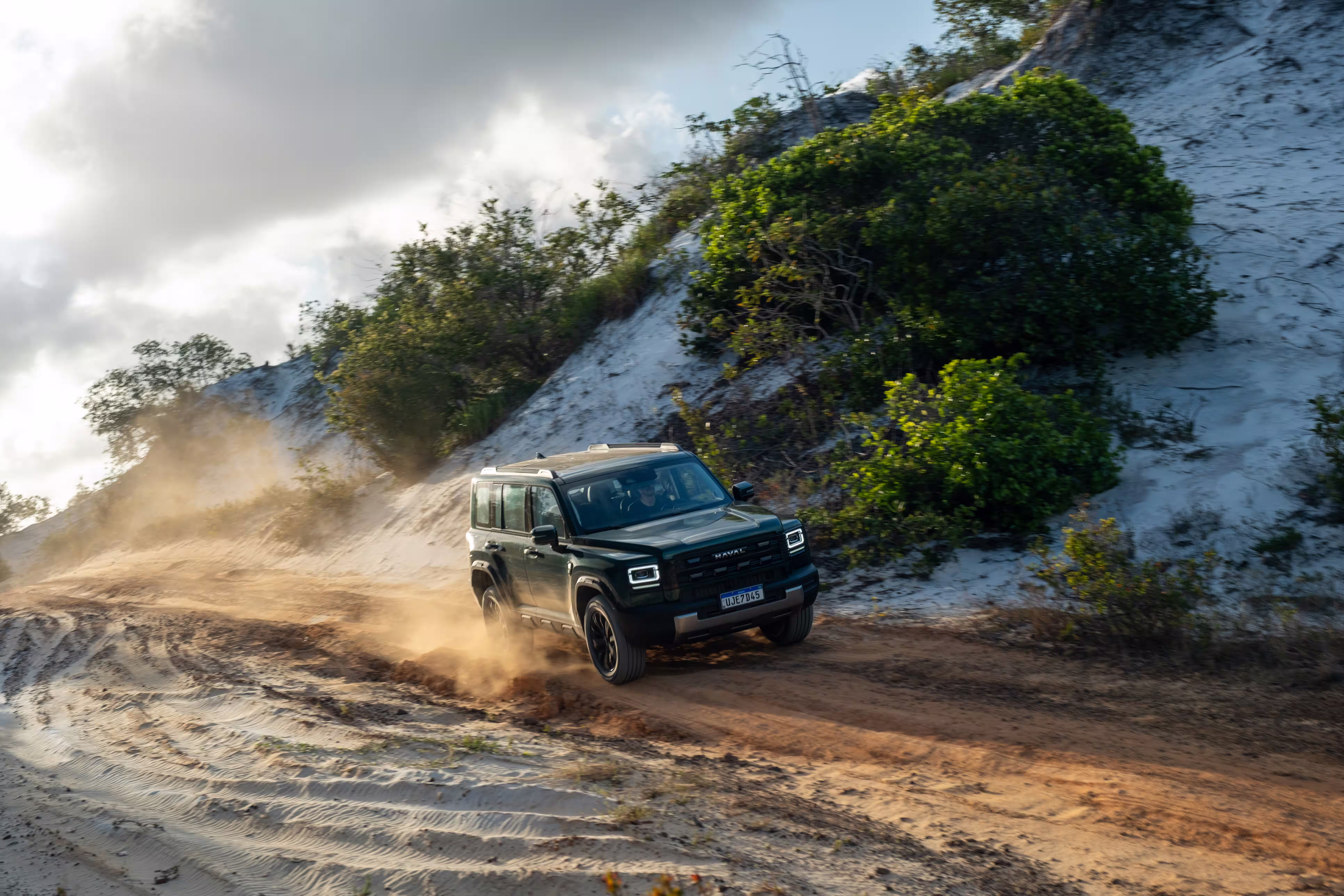 Foto de divulgação: Haval H7 verde em movimento numa estrada de terra, com poeira iluminada atrás.