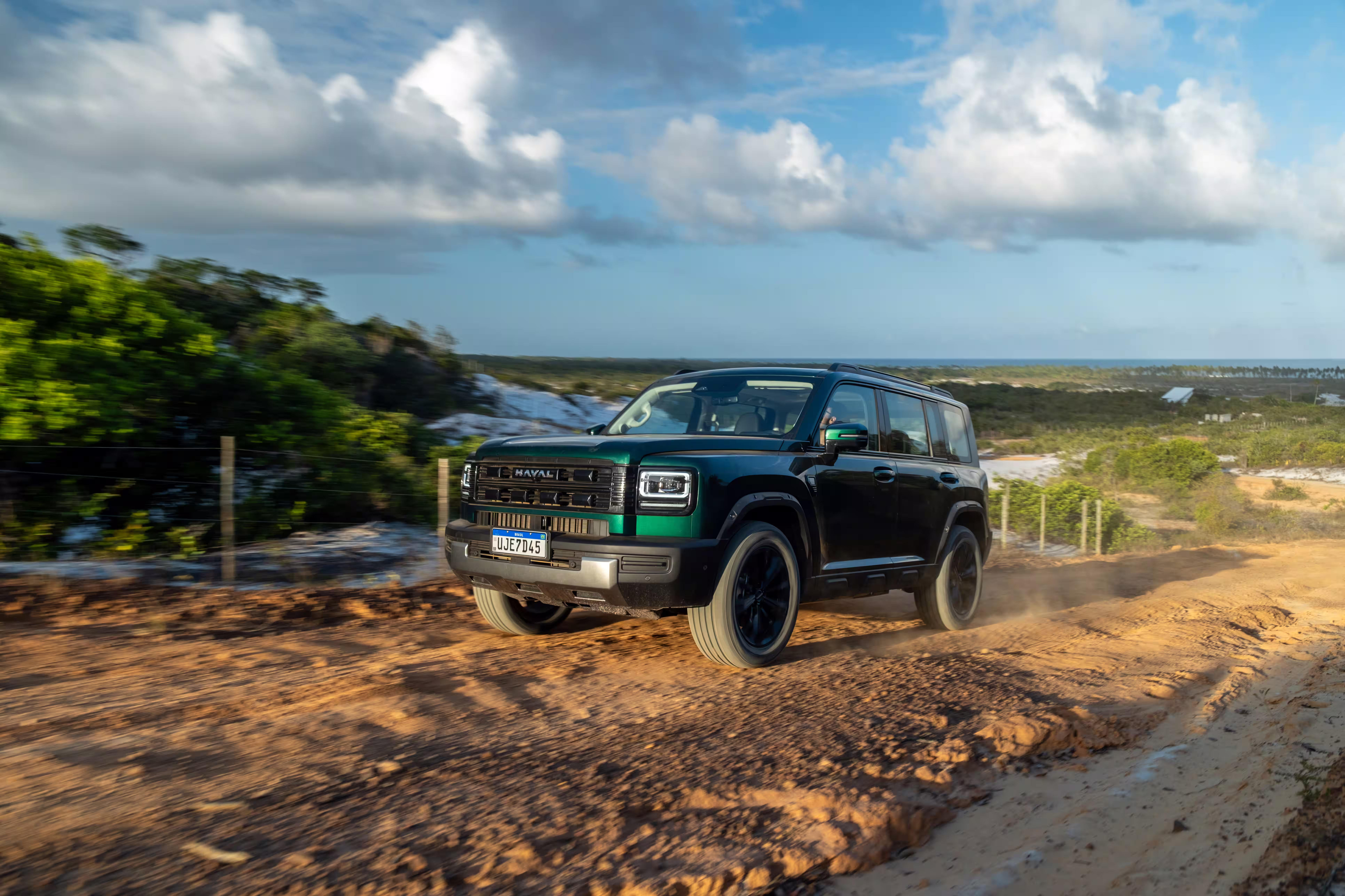 Foto de divulgação: Haval H7 verde em três quartos dianteiros numa trilha de terra cercada por vegetação baixa.