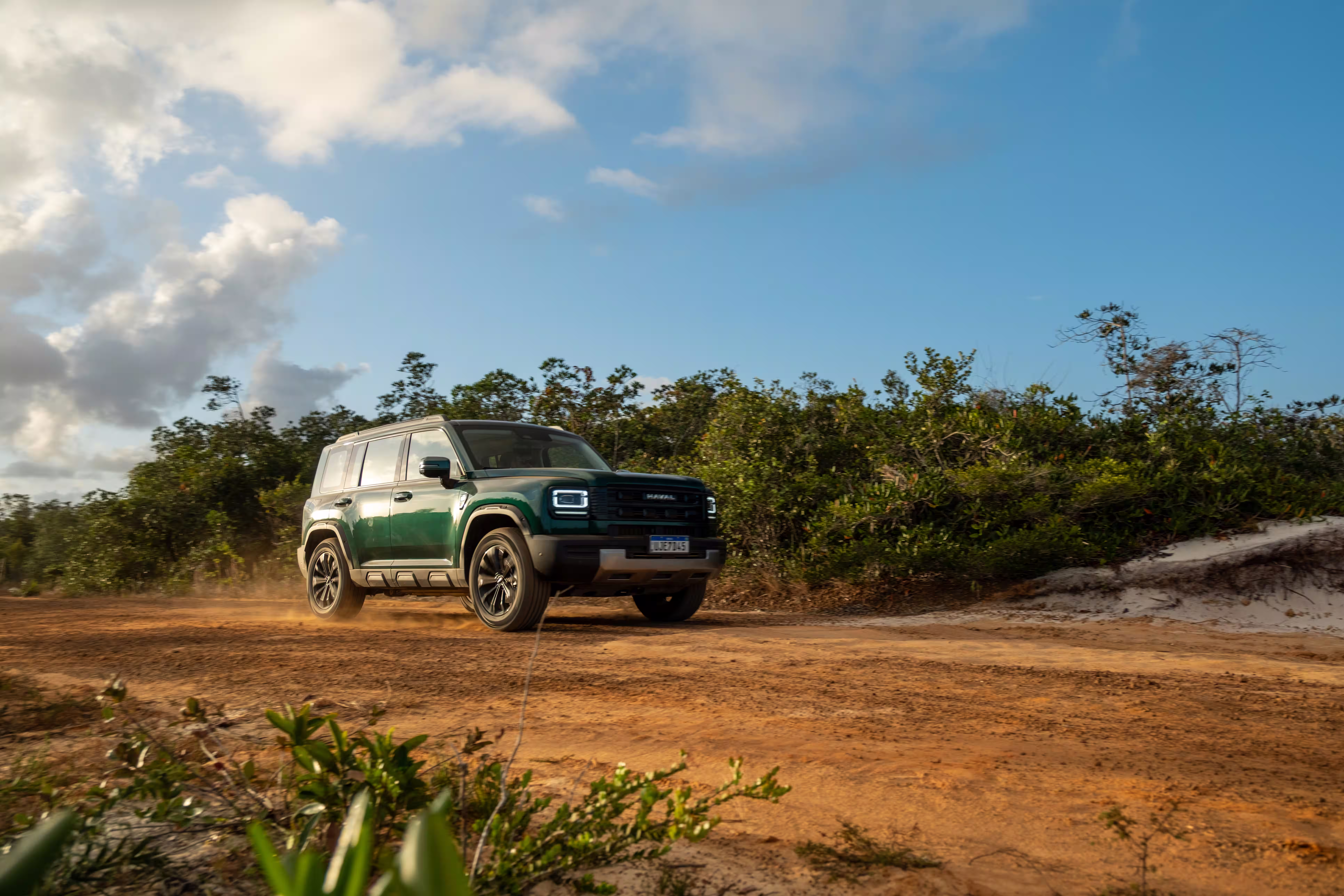 Foto de divulgação: Haval H7 verde em três quartos dianteiros numa trilha de terra sob luz de fim de tarde.