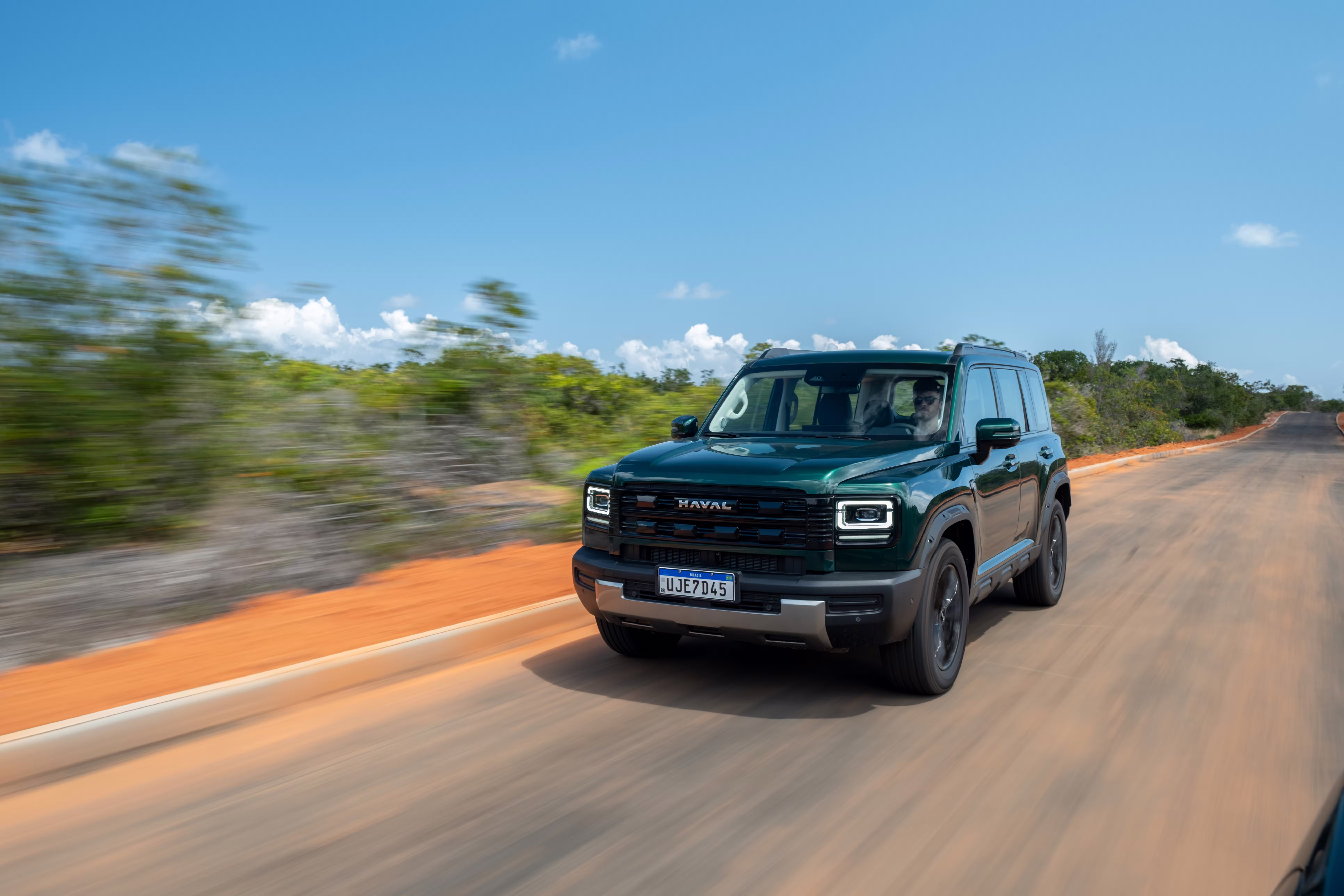 Foto de divulgação: Haval H7 verde em movimento no asfalto, com vegetação desfocada ao lado.