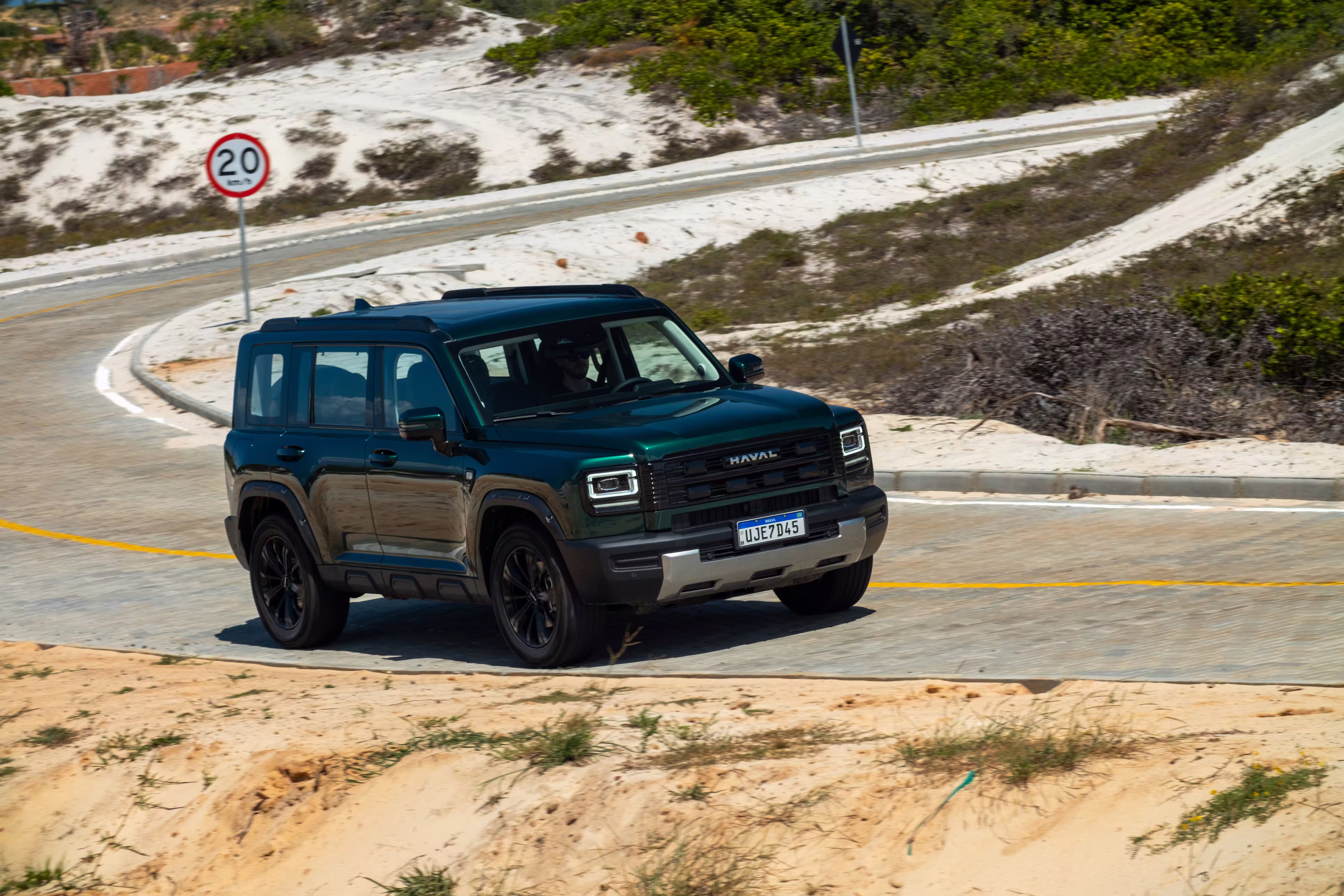 Foto de divulgação: Haval H7 verde em três quartos dianteiros numa curva de asfalto fotografada de cima.