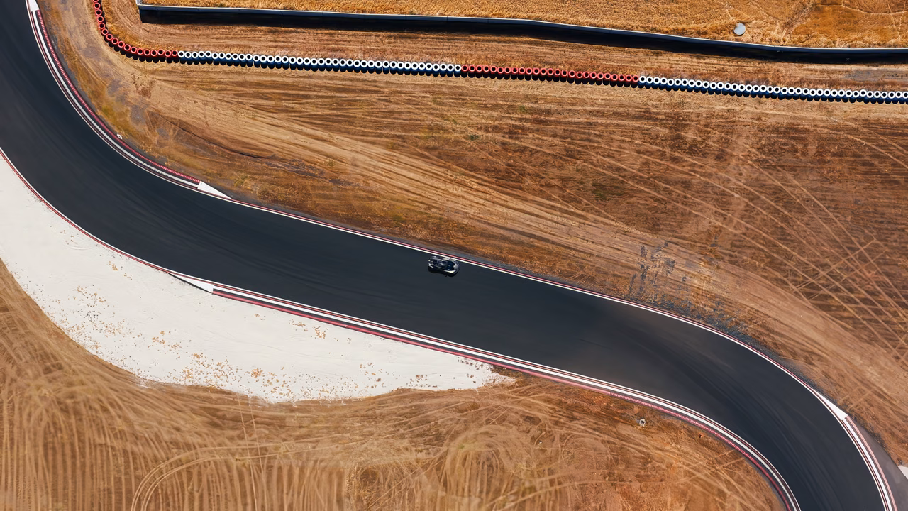 Vista aérea do Bugatti Tourbillon percorrendo uma curva entre áreas de terra seca