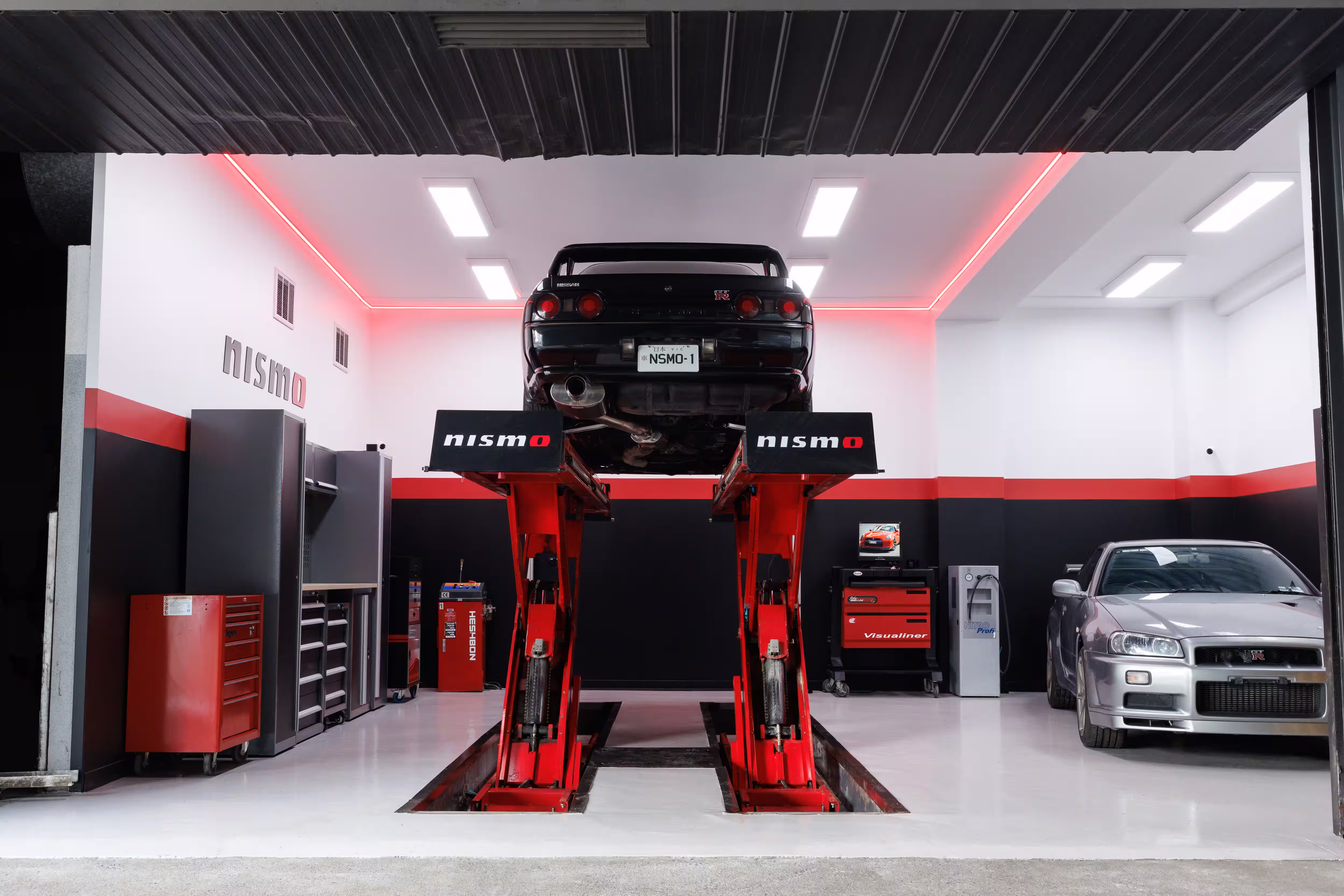 Skyline GT-R preto elevado na oficina Nismo com outro GT-R prata ao lado