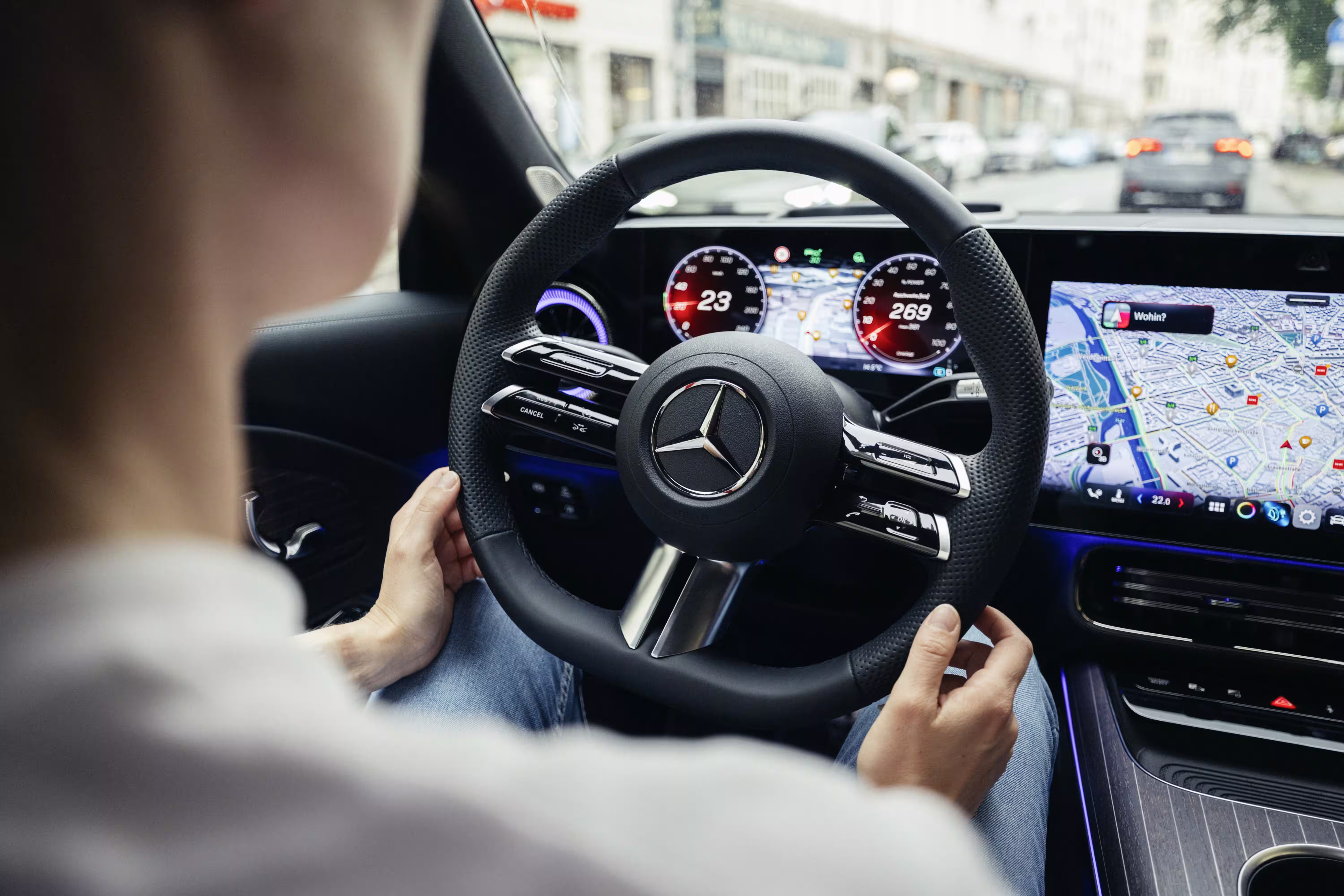 Volante de um Mercedes-Benz segurado pelo motorista com instrumentos digitais e navegação ao fundo