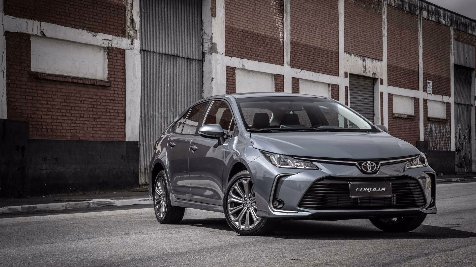 Toyota Corolla 2020 cinza visto em três quartos dianteiros diante de edifício de tijolos
